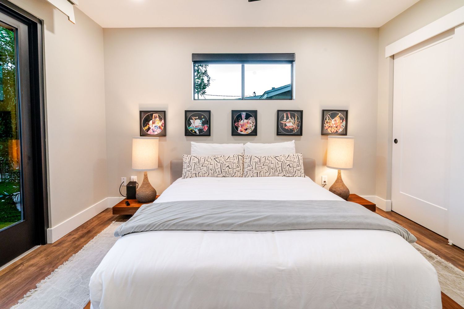 Modern bedroom interior with white walls, hardwood floors, and sliding glass doors leading to outdoor space.