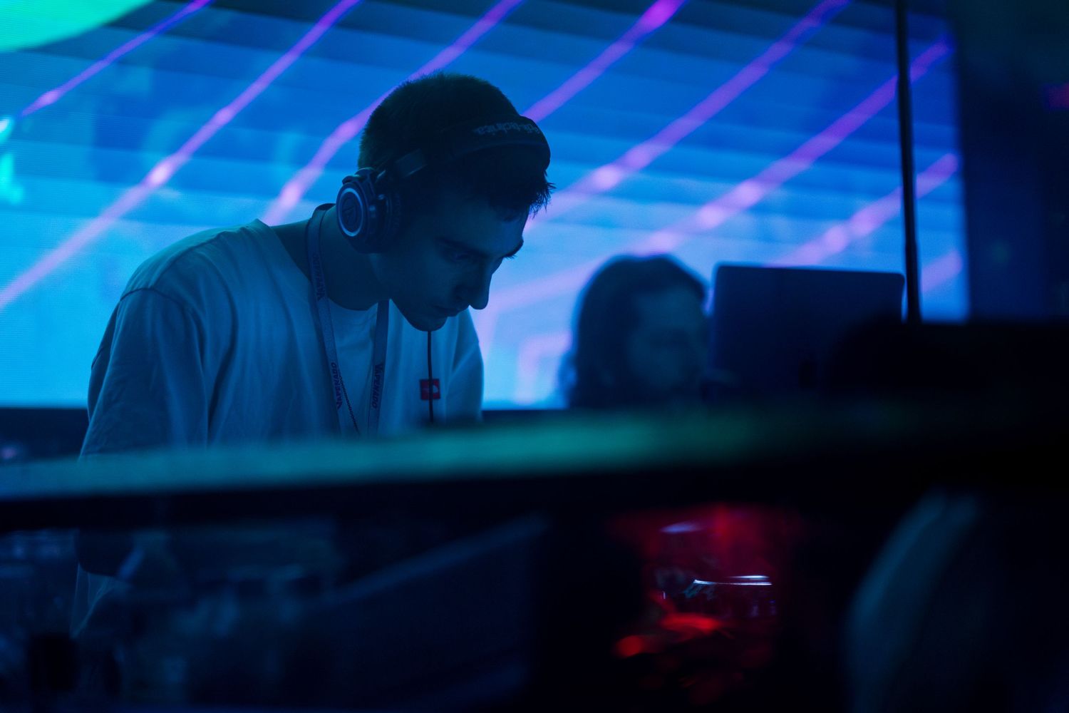 DJ performing at a nightclub with blue neon lighting and laser effects in the background.