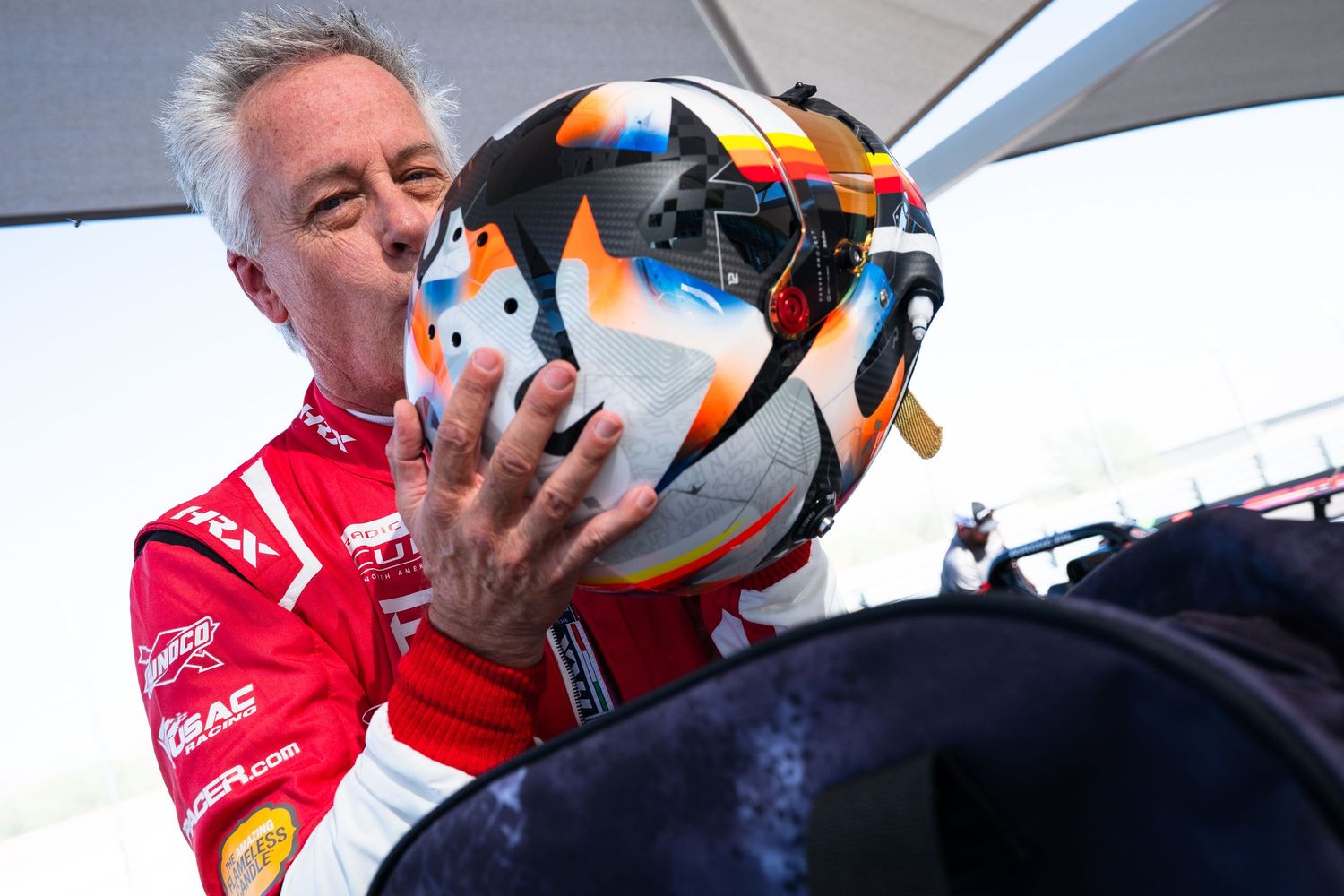 Racing driver in a red suit preparing for competition with helmet visor up.