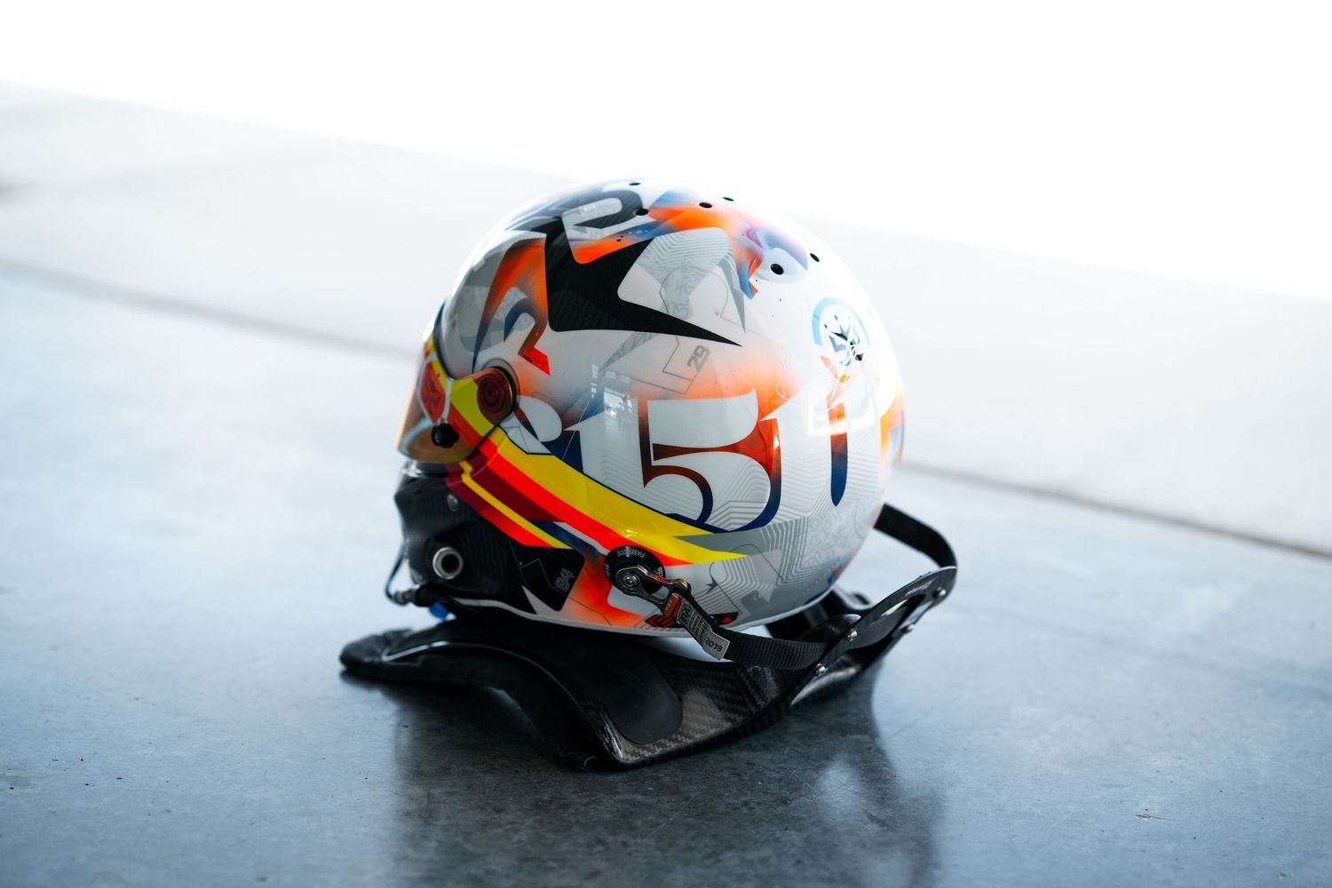 White and orange racing helmets with reflective visors displayed in sequence on light surface.