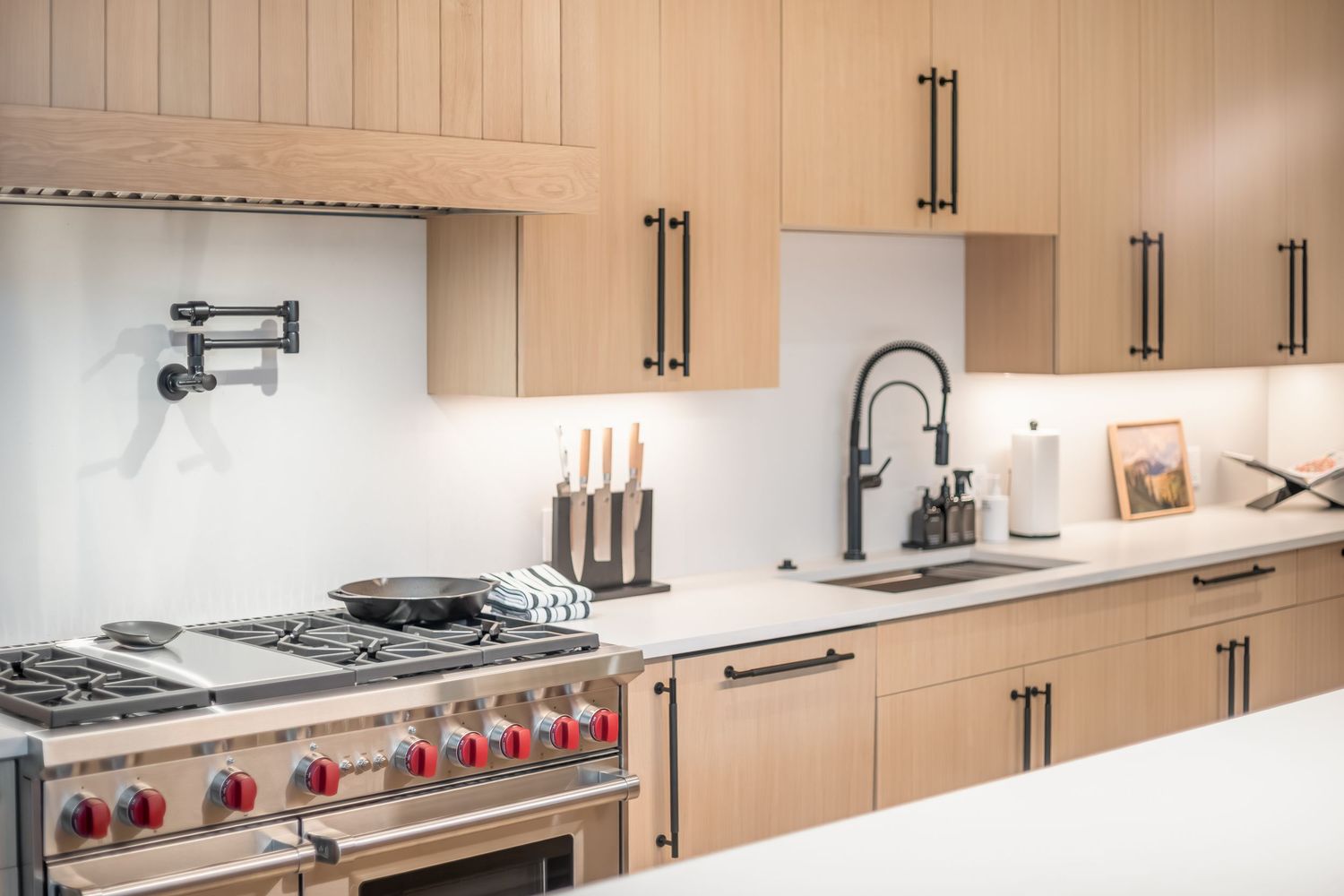 Modern light wood kitchen with stainless steel appliances and long white countertops features sleek cabinet hardware.