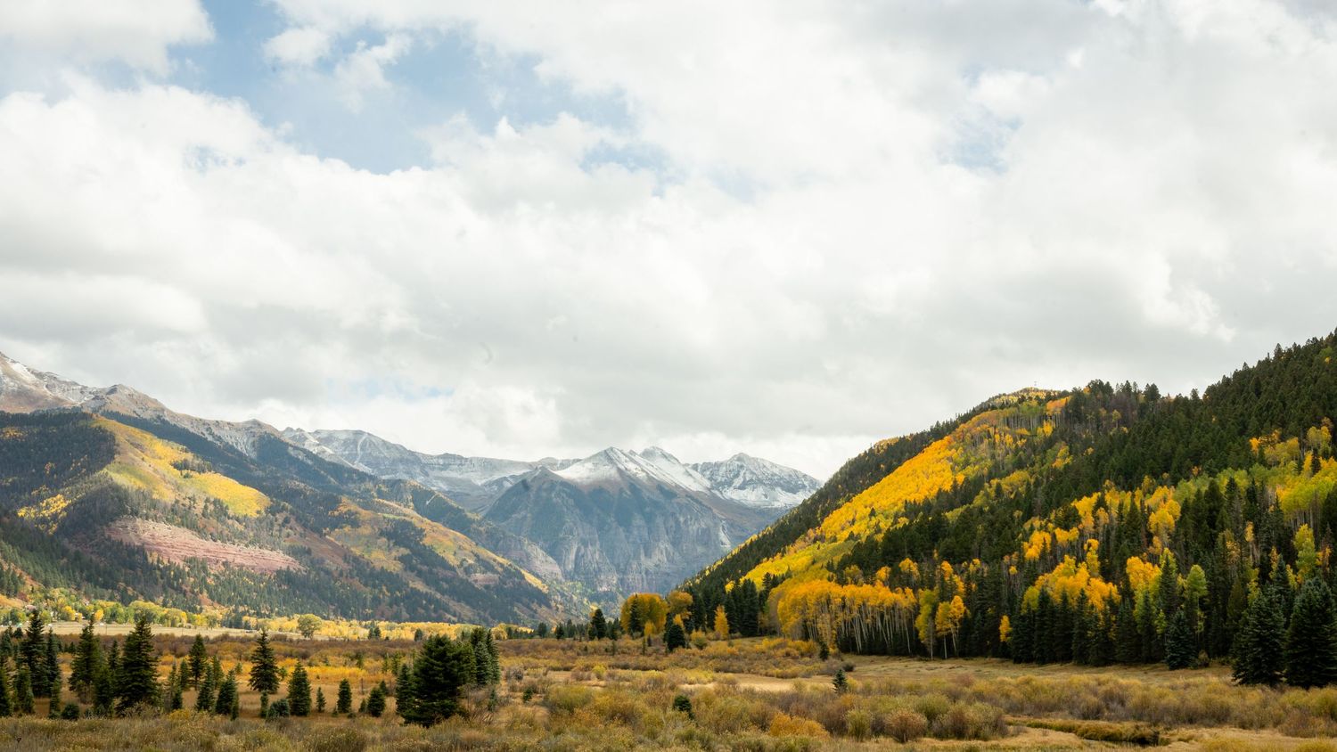 Panoramic mountain landscape with autumn colors and cloudy skies.
