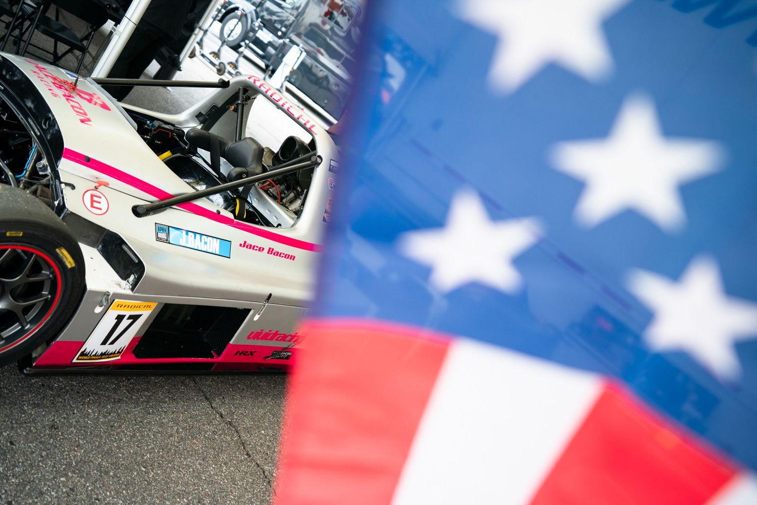 Racing car with American flag elements visible in the background during a motorsport event.