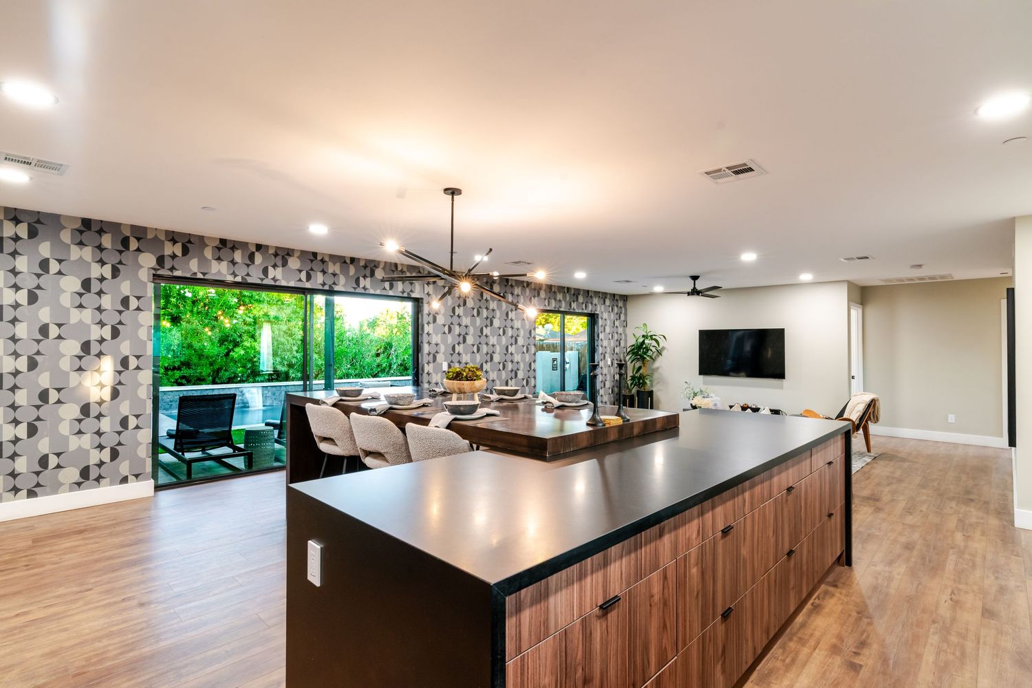 Contemporary basement bar area with wood cabinetry, black countertops, and recessed lighting creates an elegant entertainment space.