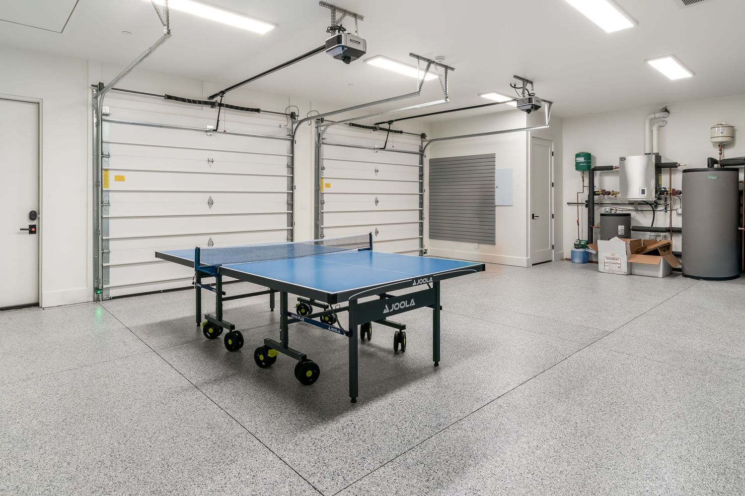 Spacious white garage with epoxy flooring features ping pong tables and storage solutions.