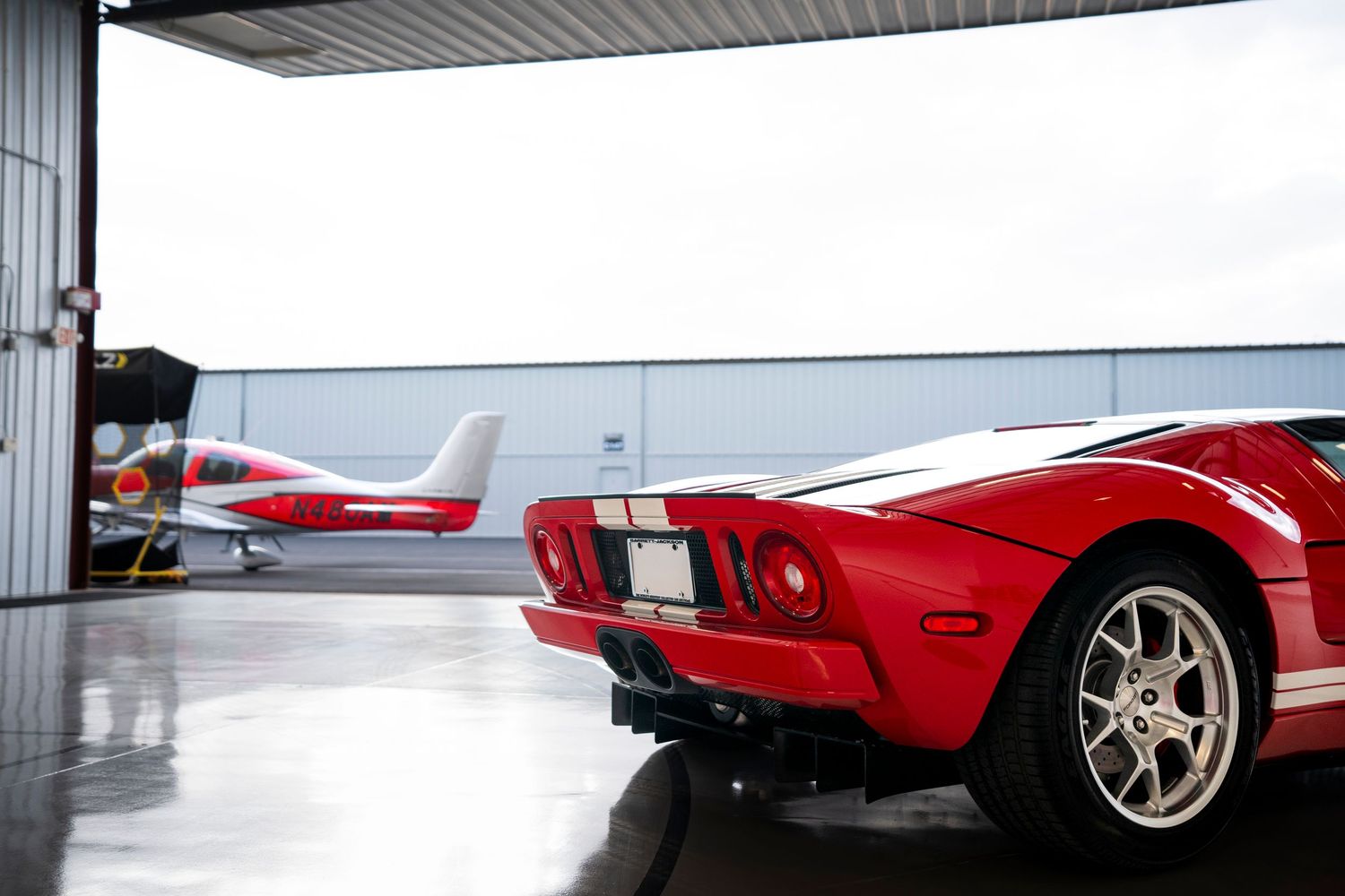 Wide panoramic view of red sports car in white industrial garage space.