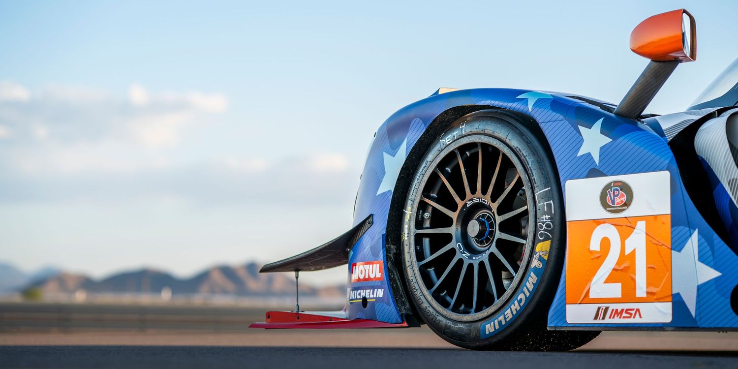 Side profile of prototype race cars with distinctive green and red liveries at dusk.