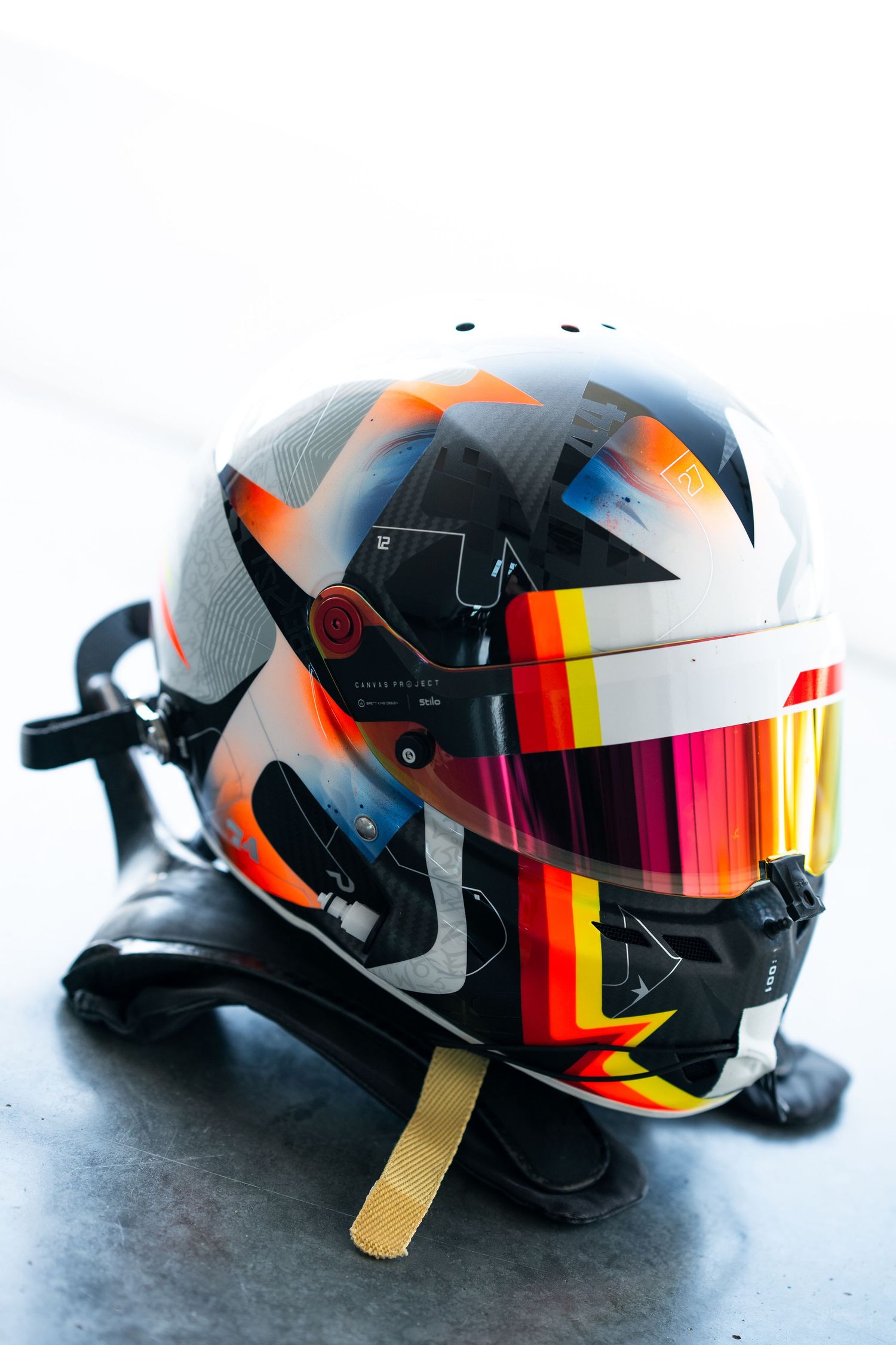 Racing helmet with orange accents and reflective visor shown from multiple angles on dark surface.