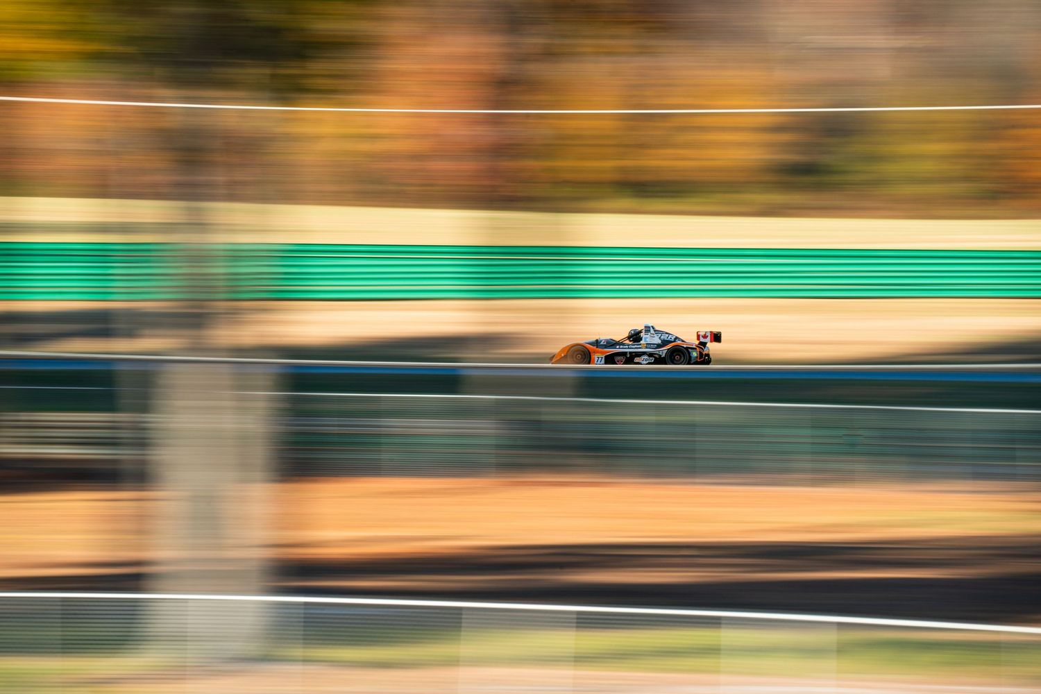 Motion-blurred racetrack with barriers and catch fencing during golden hour lighting.