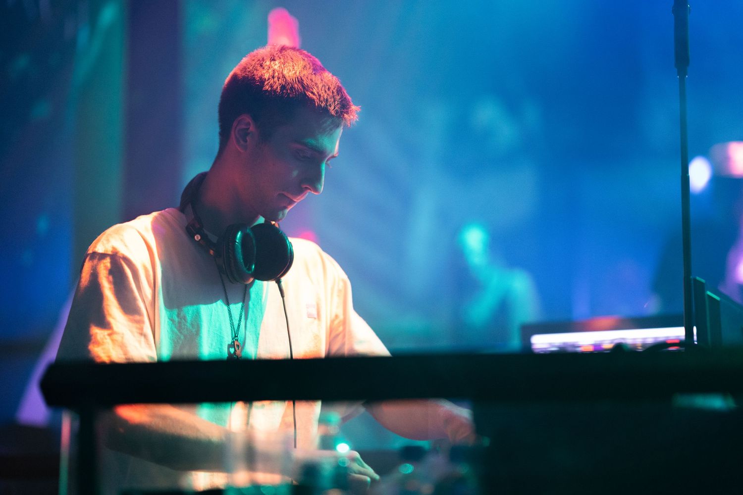 DJ performs on stage with colorful blue lighting and electronic equipment at a nightclub event.