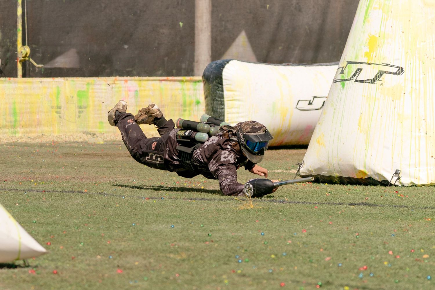 Paintball players take cover behind inflatable bunkers on a grassy field during an intense match.