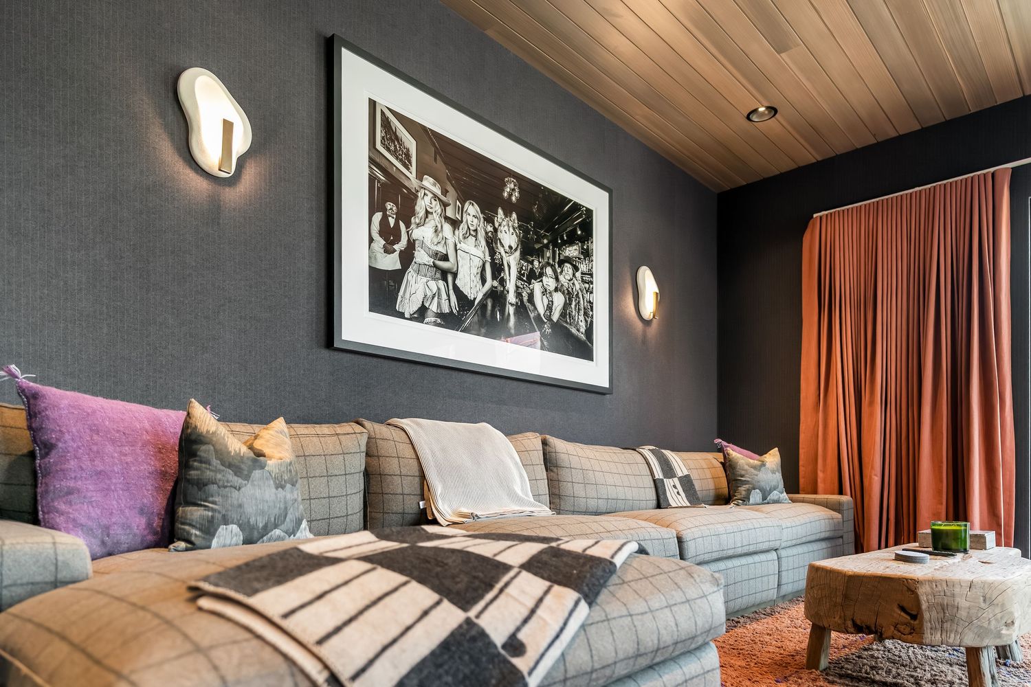 Modern media room with sectional sofa, artwork, and wood-paneled ceiling.