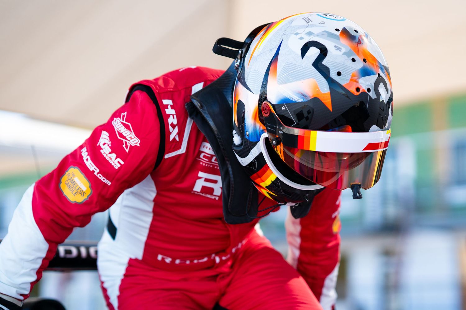 Motorcycle racer in red racing suit leans into a tight turn on a professional racing track during competition.