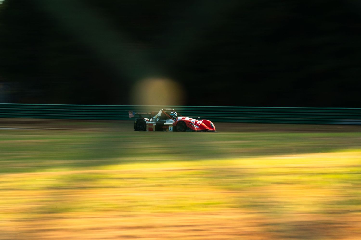 Race car speeding past autumn foliage creating motion blur effect on track.