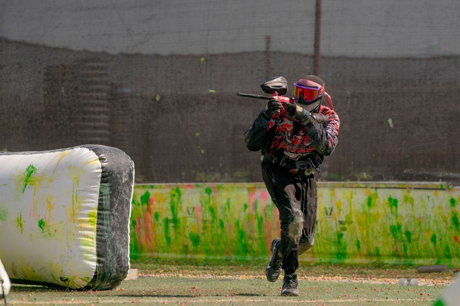 Paintball player runs past inflatable bunker on field with splattered paint.