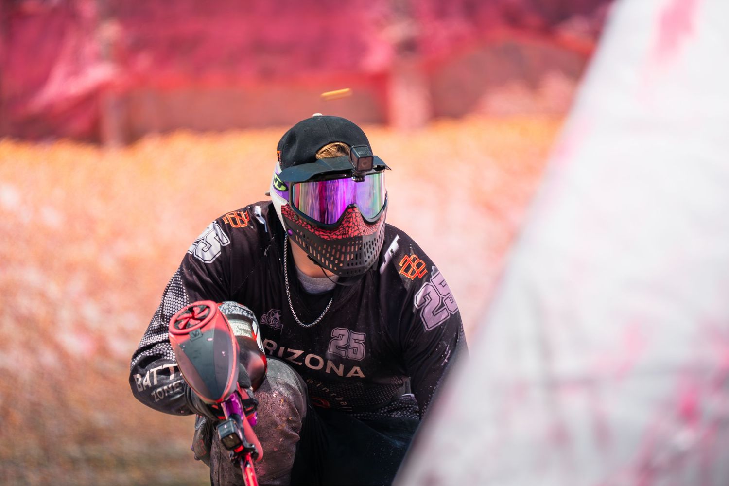 Close-up of a paintball player wearing purple iridescent goggles and Arizona jersey during a match.