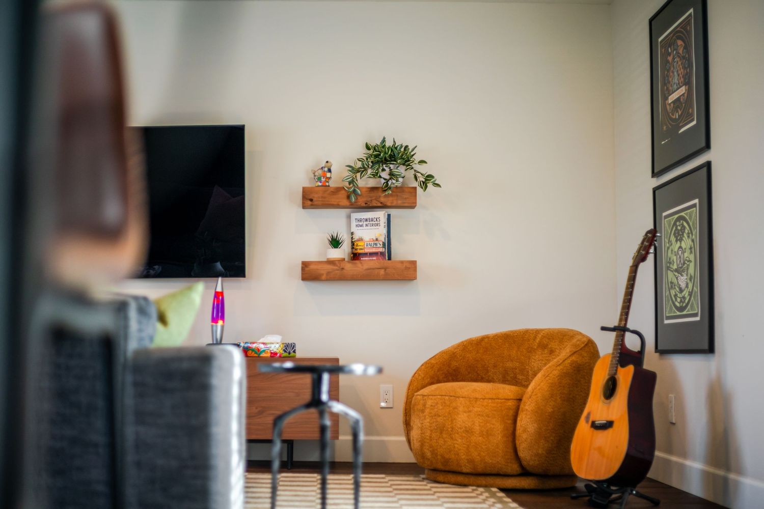 Contemporary living room with orange accent chair, acoustic guitar, and minimalist decor.