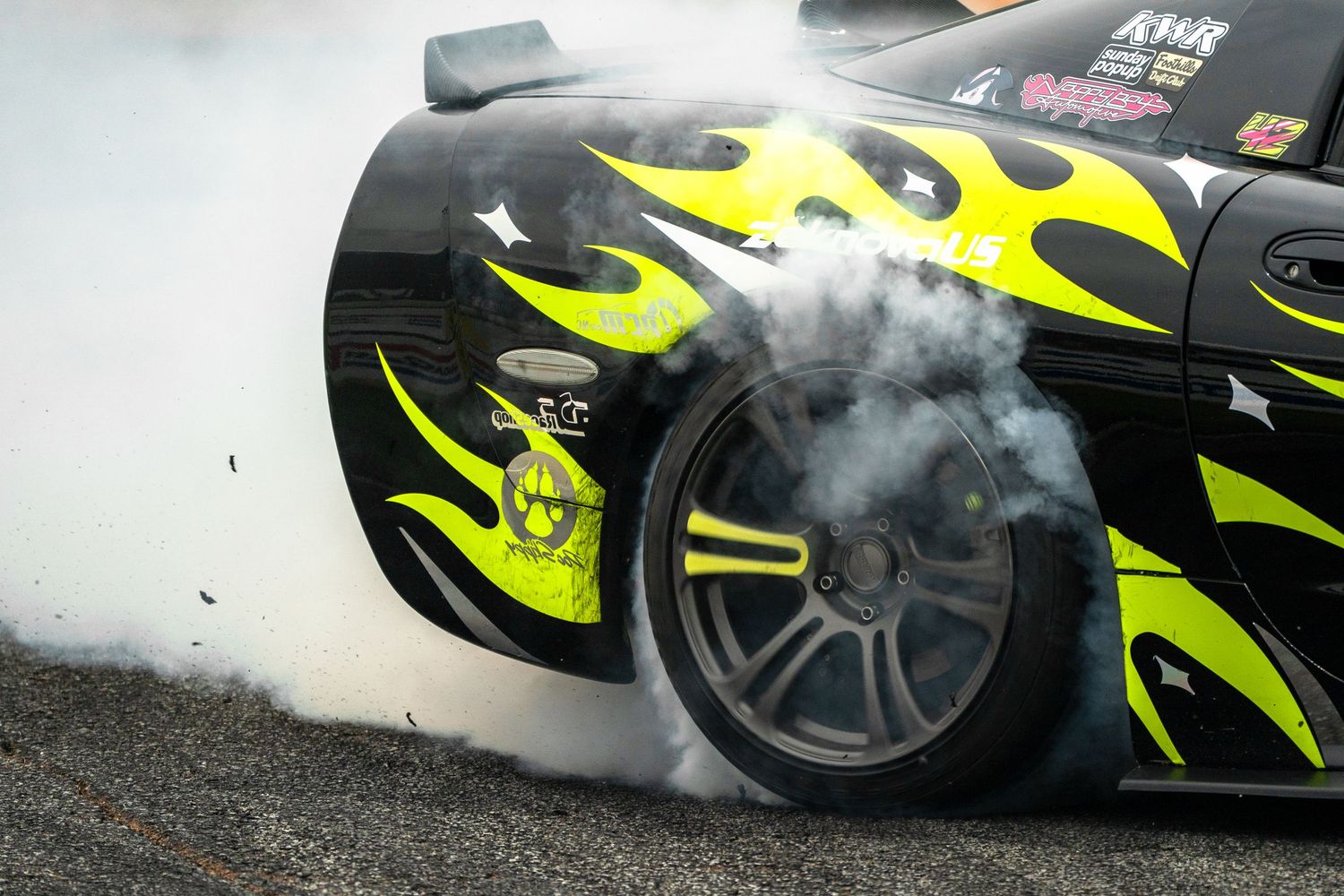 Black and yellow flame-wrapped drift car spinning tires with heavy smoke on a race track.