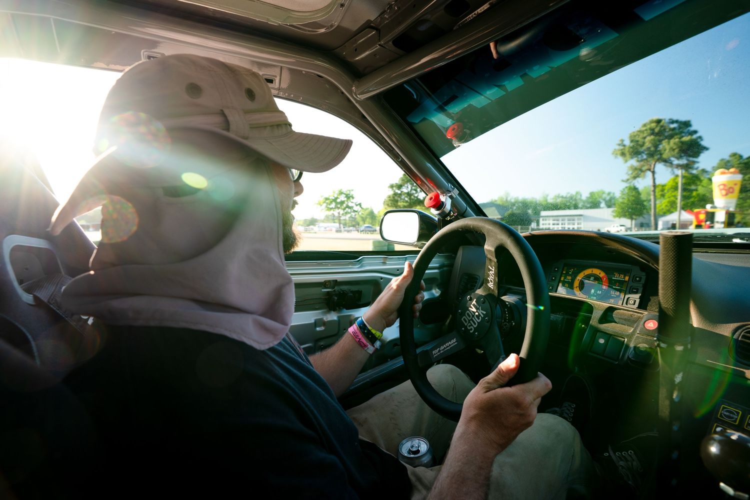 Person wearing a cap driving a vintage car, with sunlight streaming through the windshield on a sunny day.