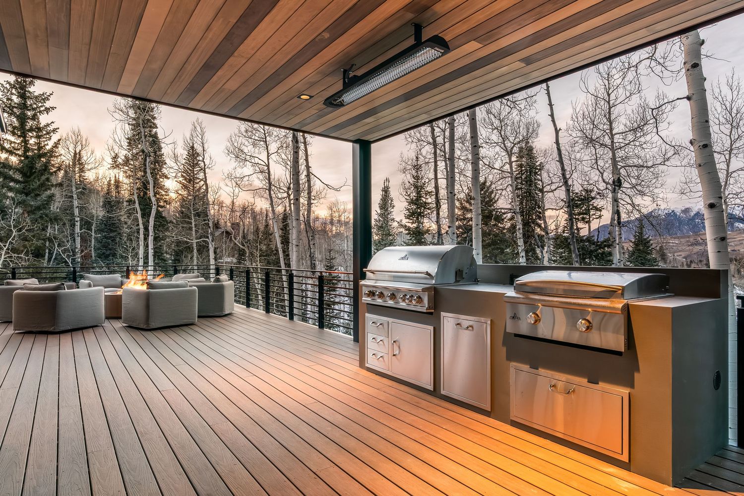 Luxurious wooden deck with glass railings and panoramic mountain views at golden hour.