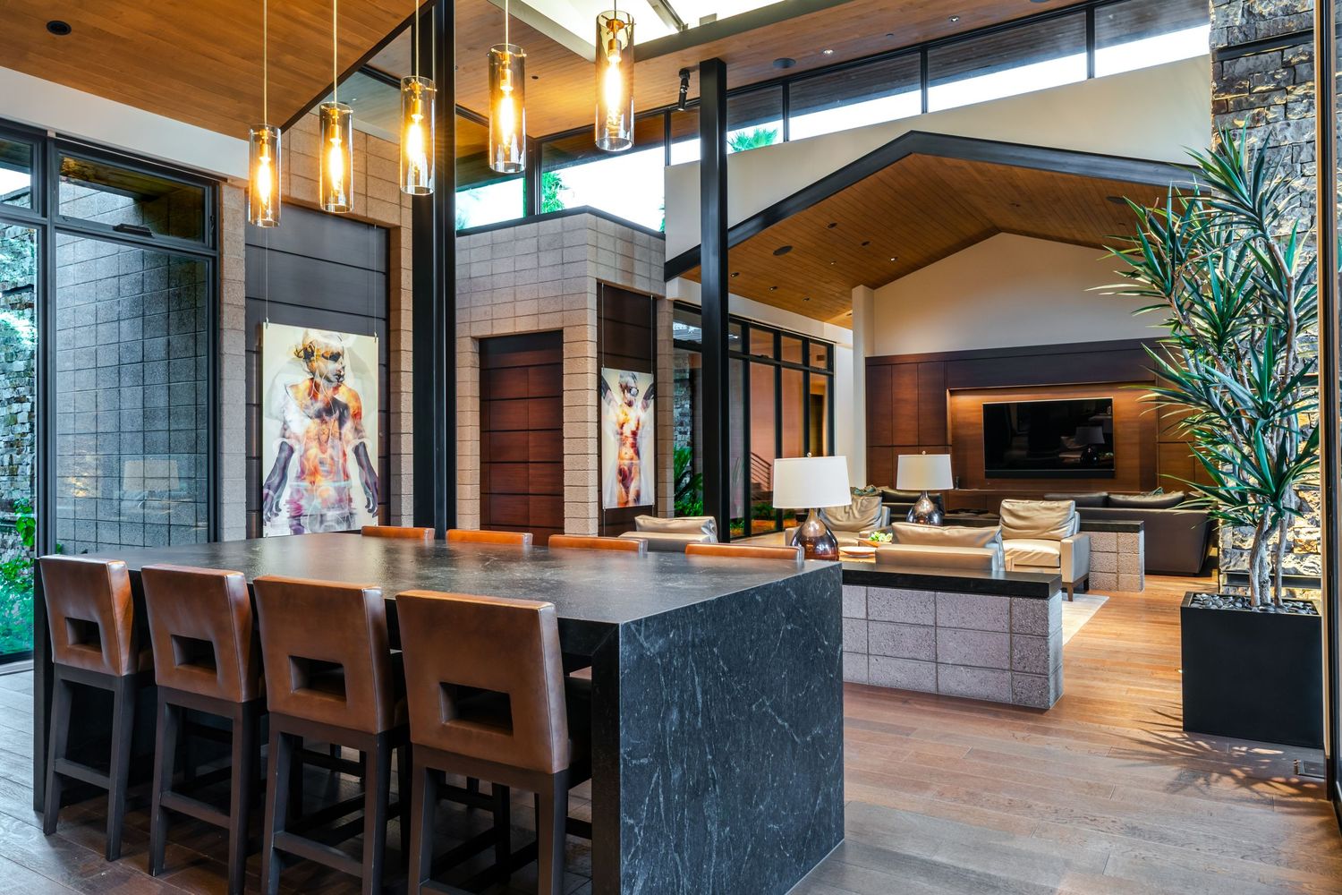 Modern open concept home interior features wood floors, black stone accents, and pendant lighting over dining area.