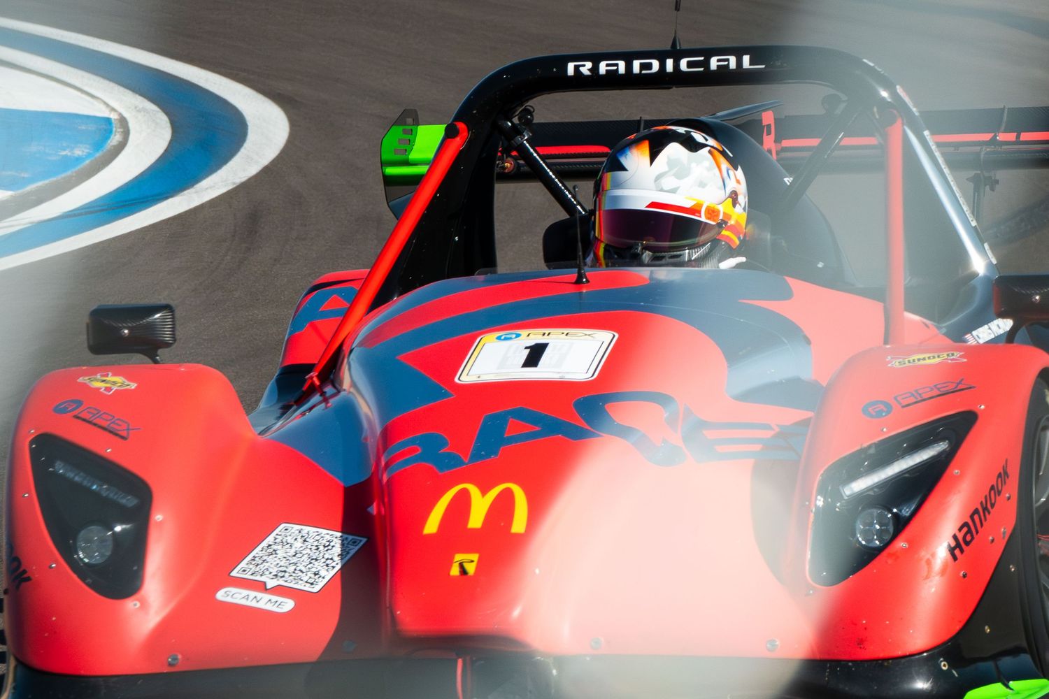 Red racing car with McDonald's branding sits in garage bay during testing session.