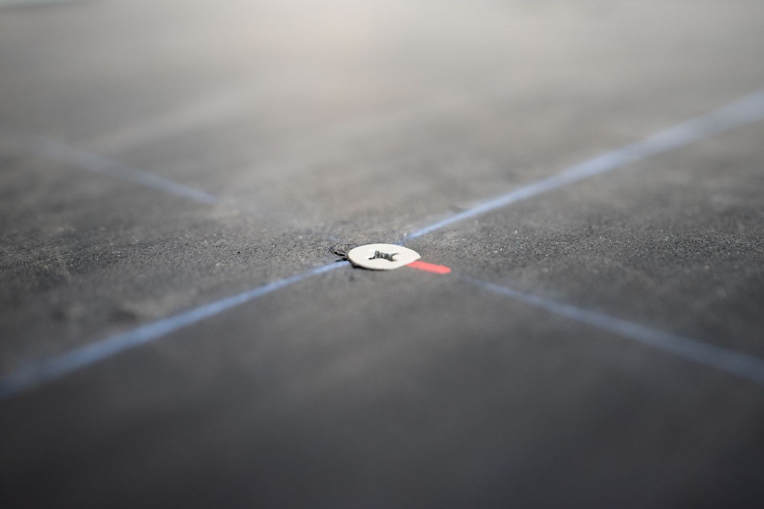Close up of a small metal marker or registration pin embedded in a dark surface with intersecting blue lines.