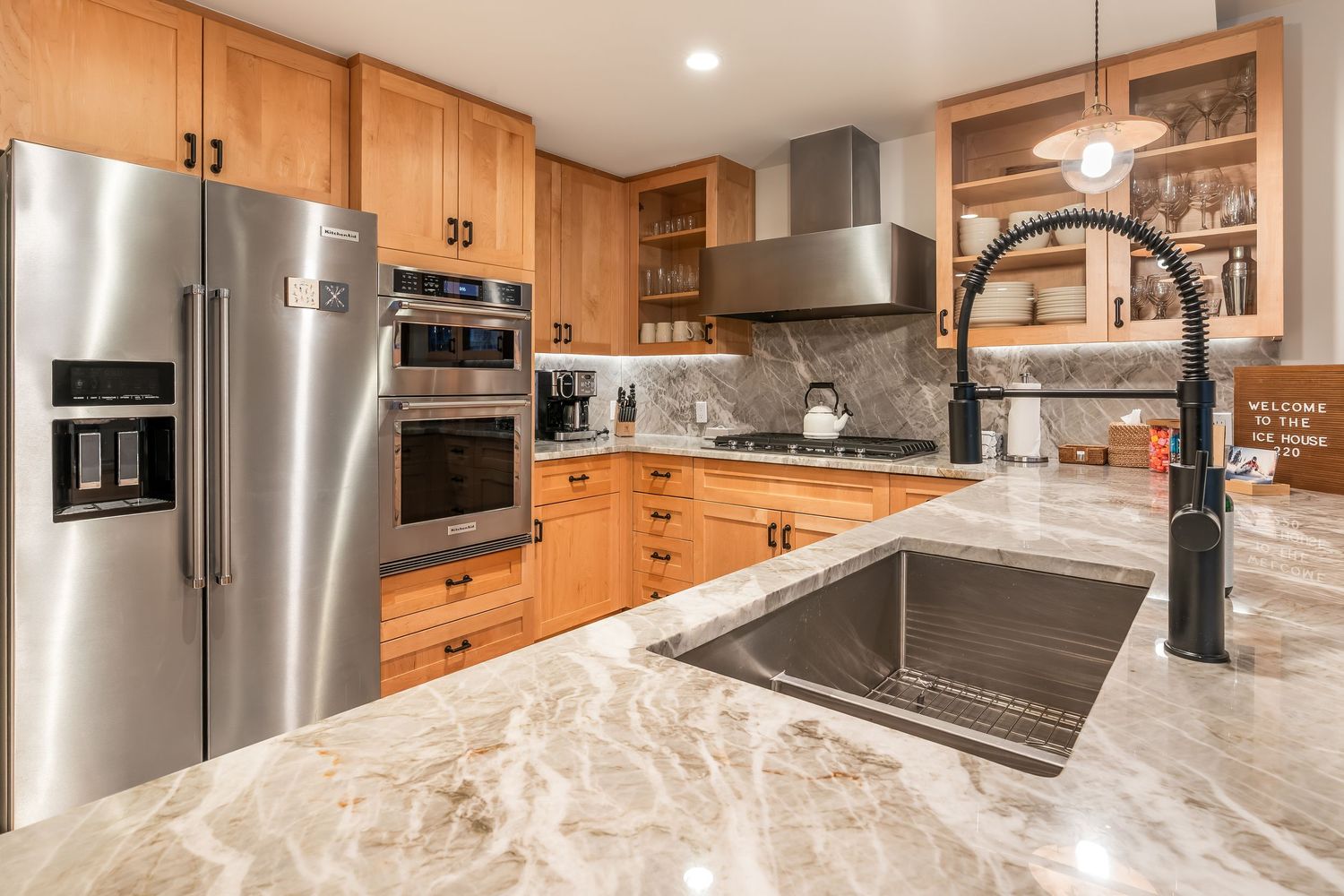 Modern kitchen with stainless steel appliances, marble countertops, wooden cabinets, and a farmhouse sink with black faucet.