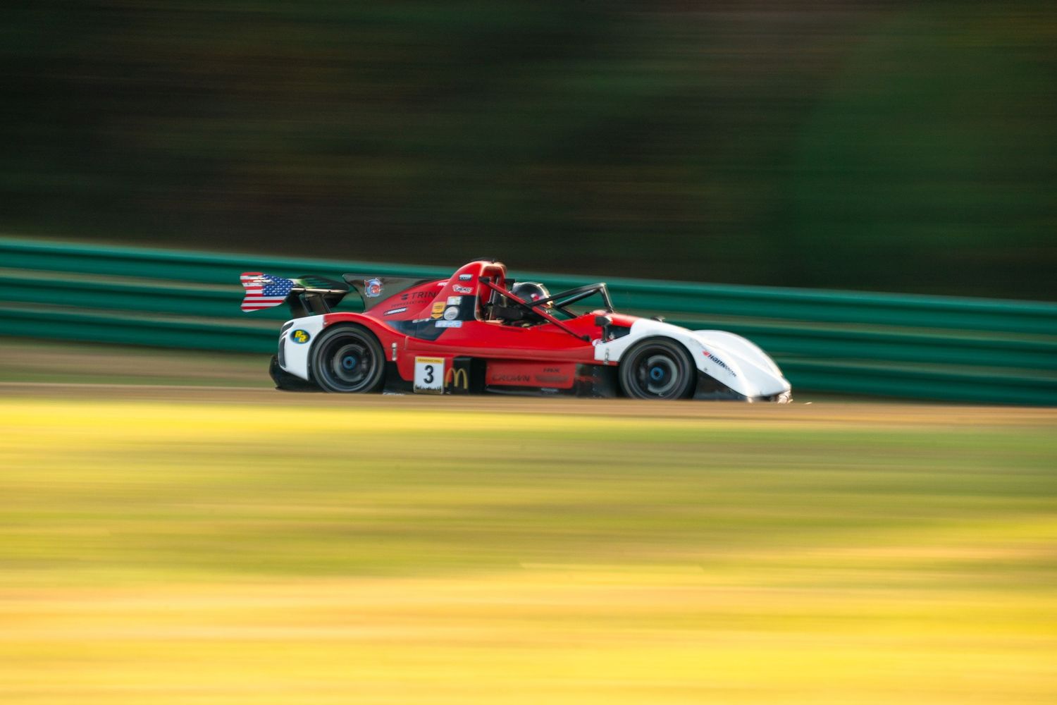 Race cars speeding past yellow and green trackside barriers during competition.