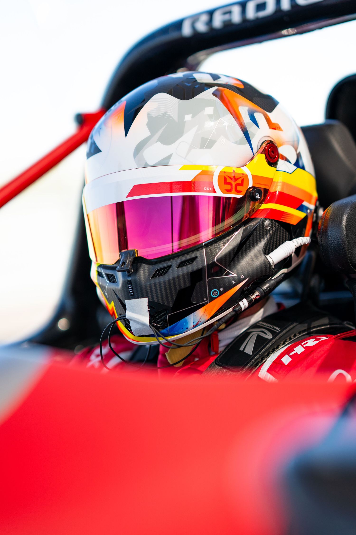 Close-up view of racing helmets in red and orange colors with reflective visors lined up in sequence.