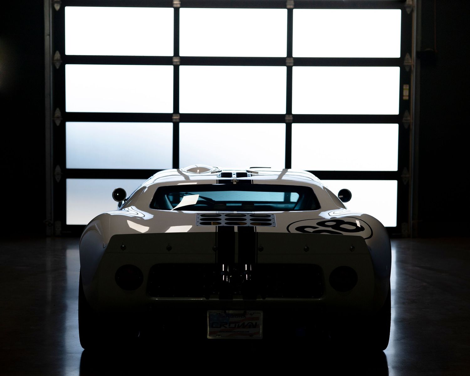 Dark silhouette of a luxury sports car in a dimly lit garage with window backlighting.