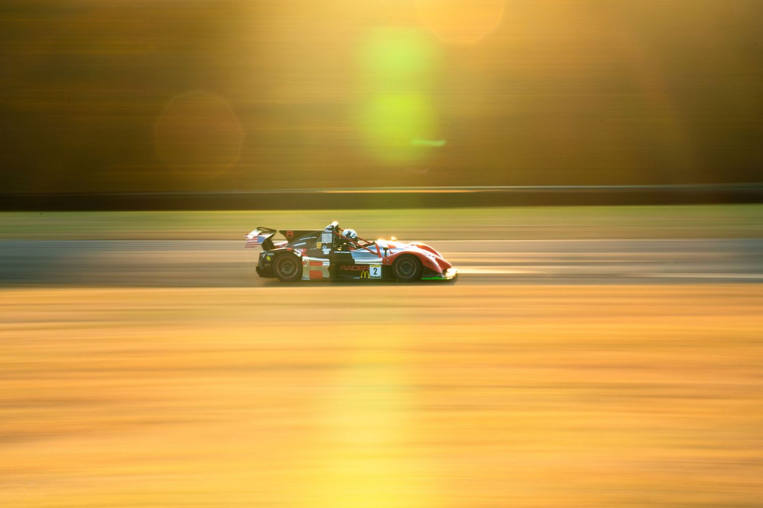 Race car speeds down track at sunset creating motion blur effect with golden light in background.