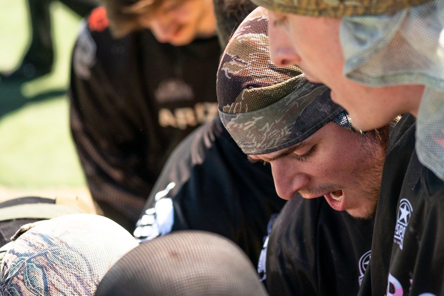 Paintball player in camouflage bandana reviews strategy during a competitive paintball tournament match.
