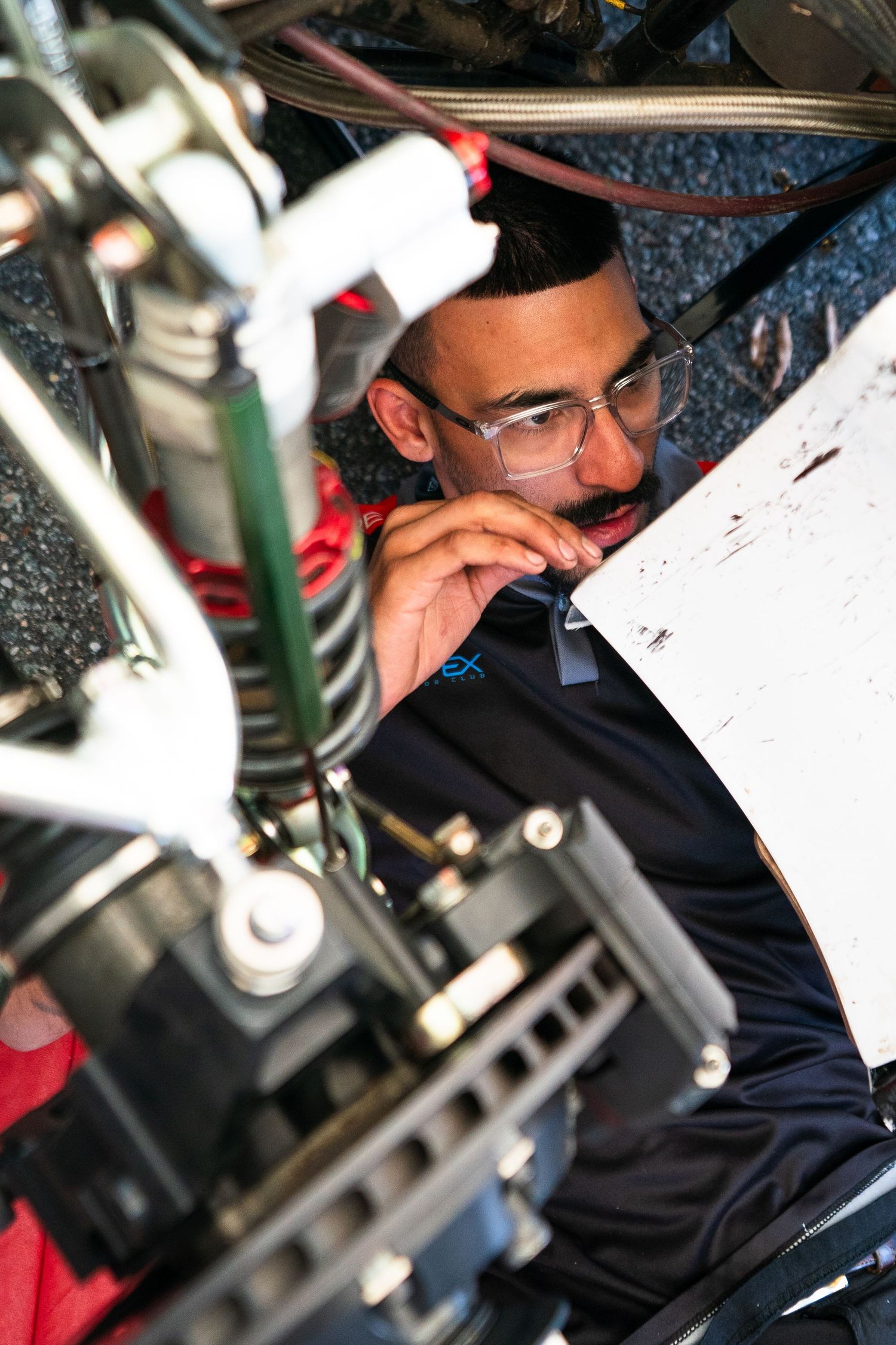 Mechanic wearing safety glasses performs detailed inspection of racing car components.