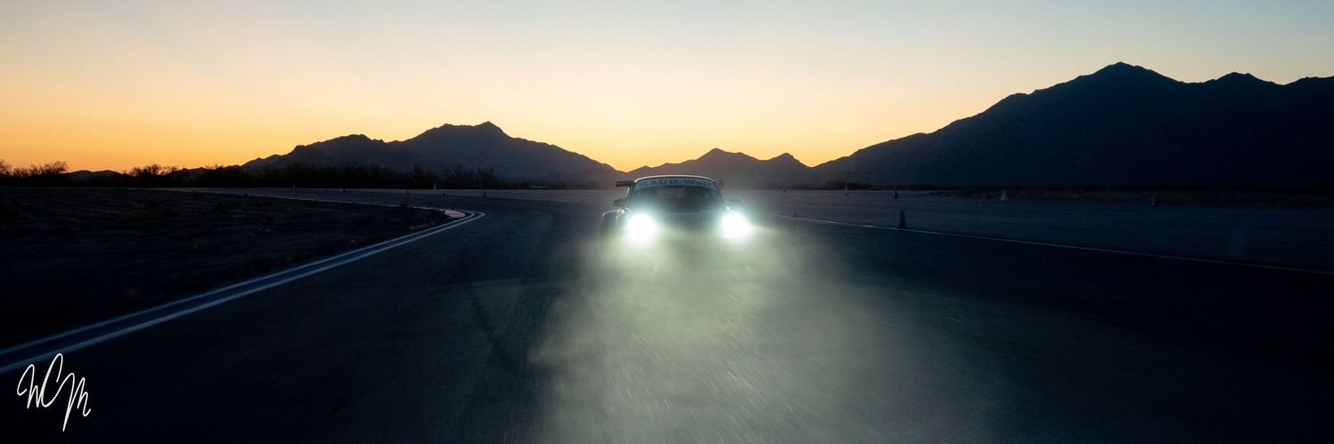 Sunset mountain road with bright car headlights illuminating asphalt.