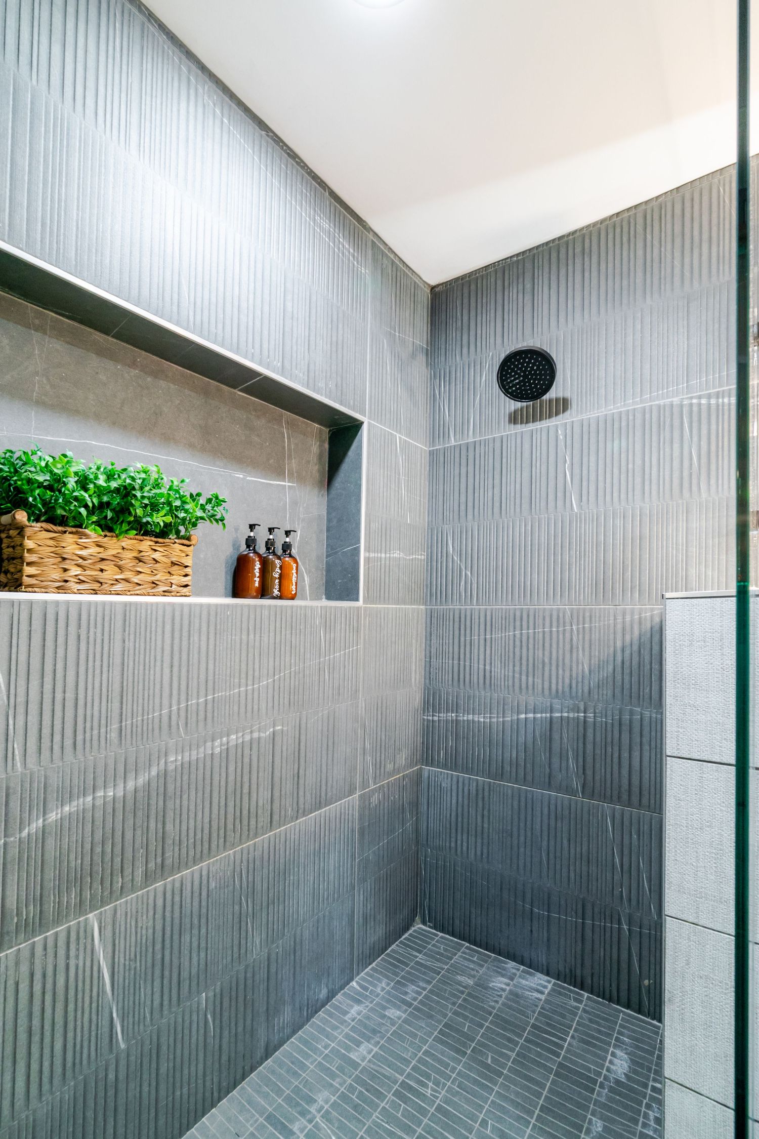 Spacious modern bathroom with grey textured tile walls and sleek rainfall shower head mounted on ceiling.