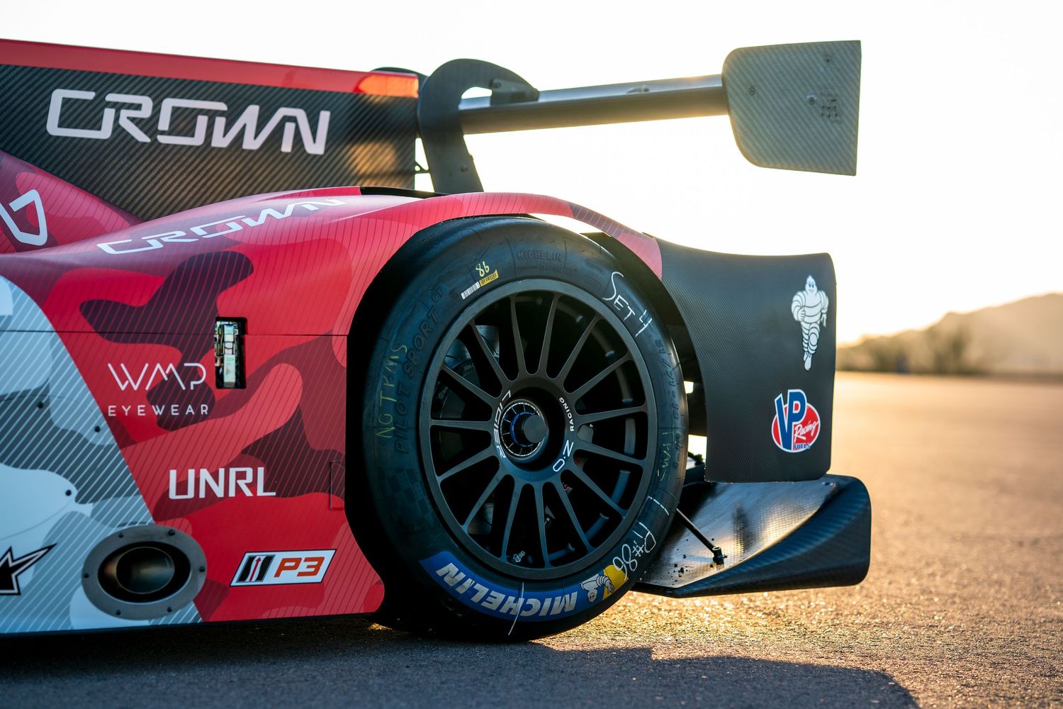 Low angle view of race car wheels and body panels against desert landscape.