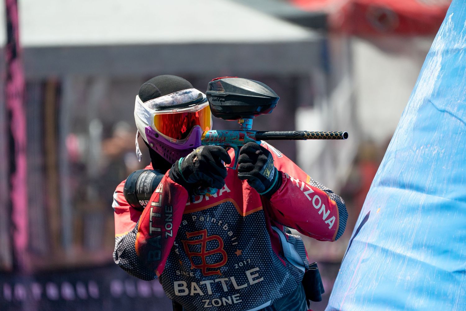 Two paintball players in masks and Battle Zone jerseys aiming during match.