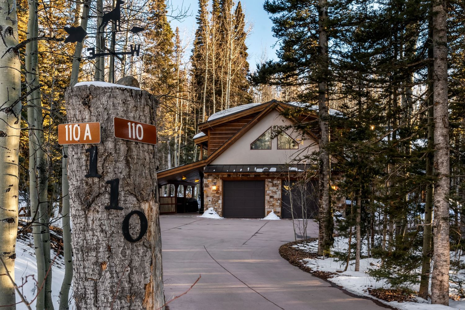 Exterior view of a rustic cabin surrounded by tall pine trees and snow in a winter forest setting.