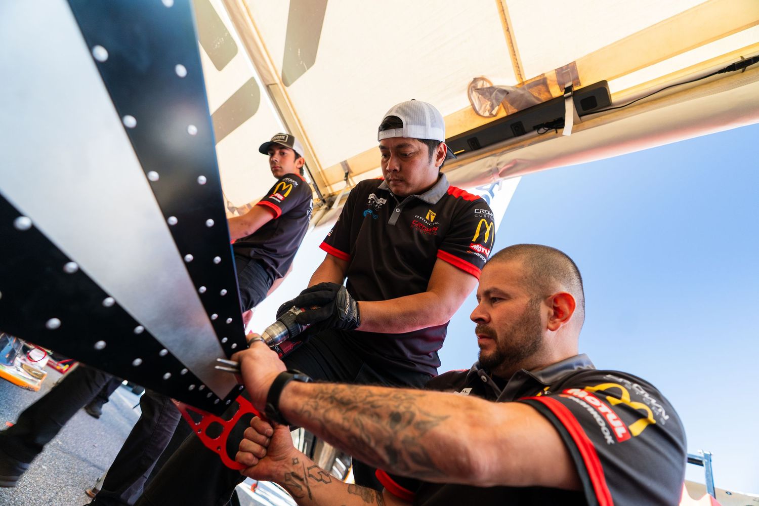 Racing team members make adjustments and preparations in the pit area during a motorsport event.