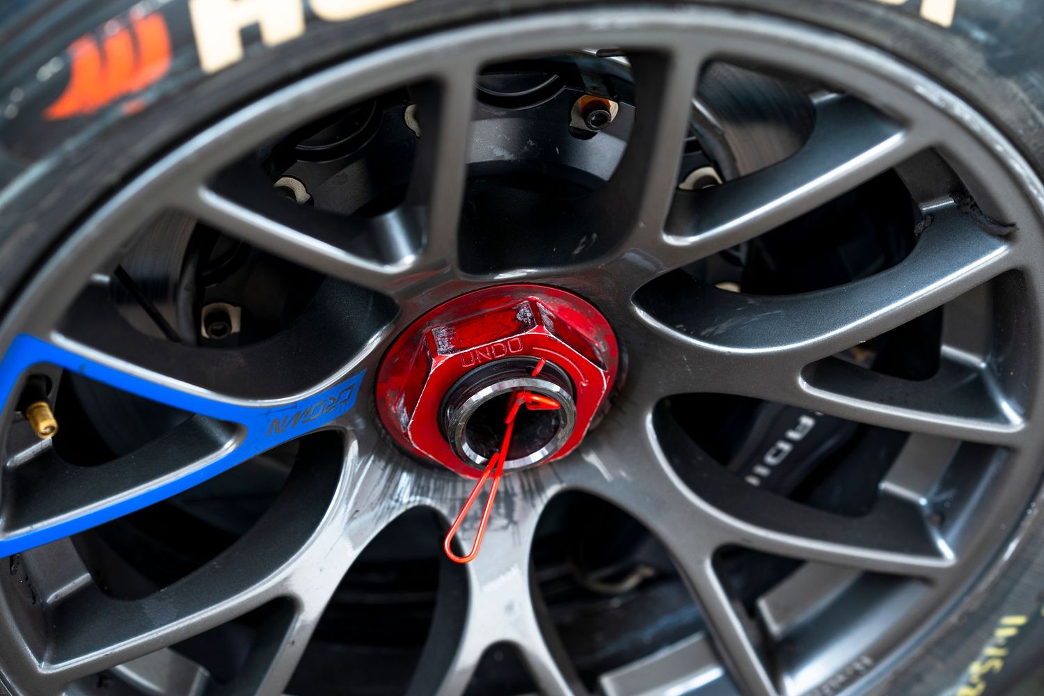 Close-up detail of alloy car wheels with red brake calipers and blue brake lines visible through the spokes.
