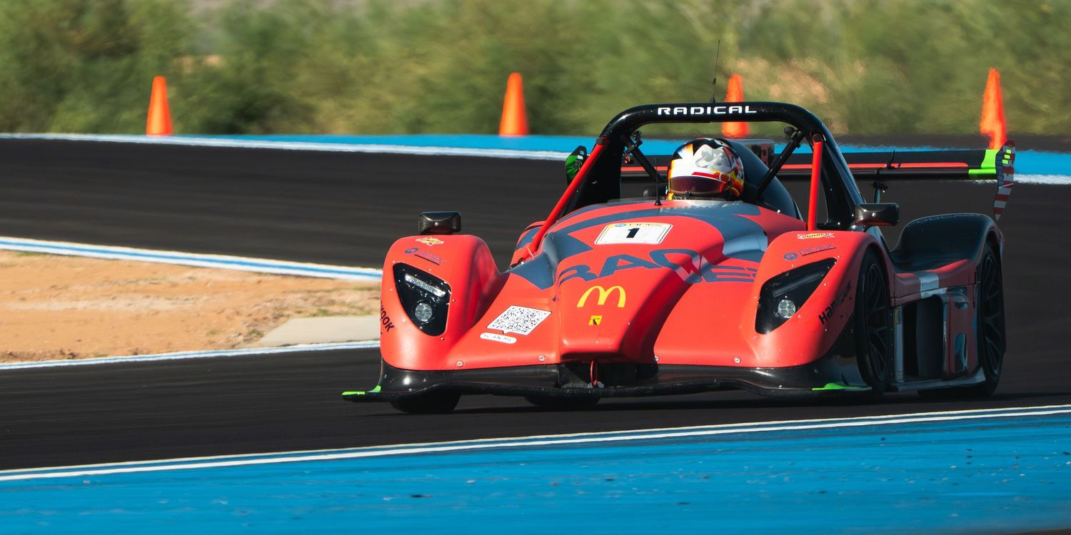Red racing cars competing on a professional race track with blue barriers.