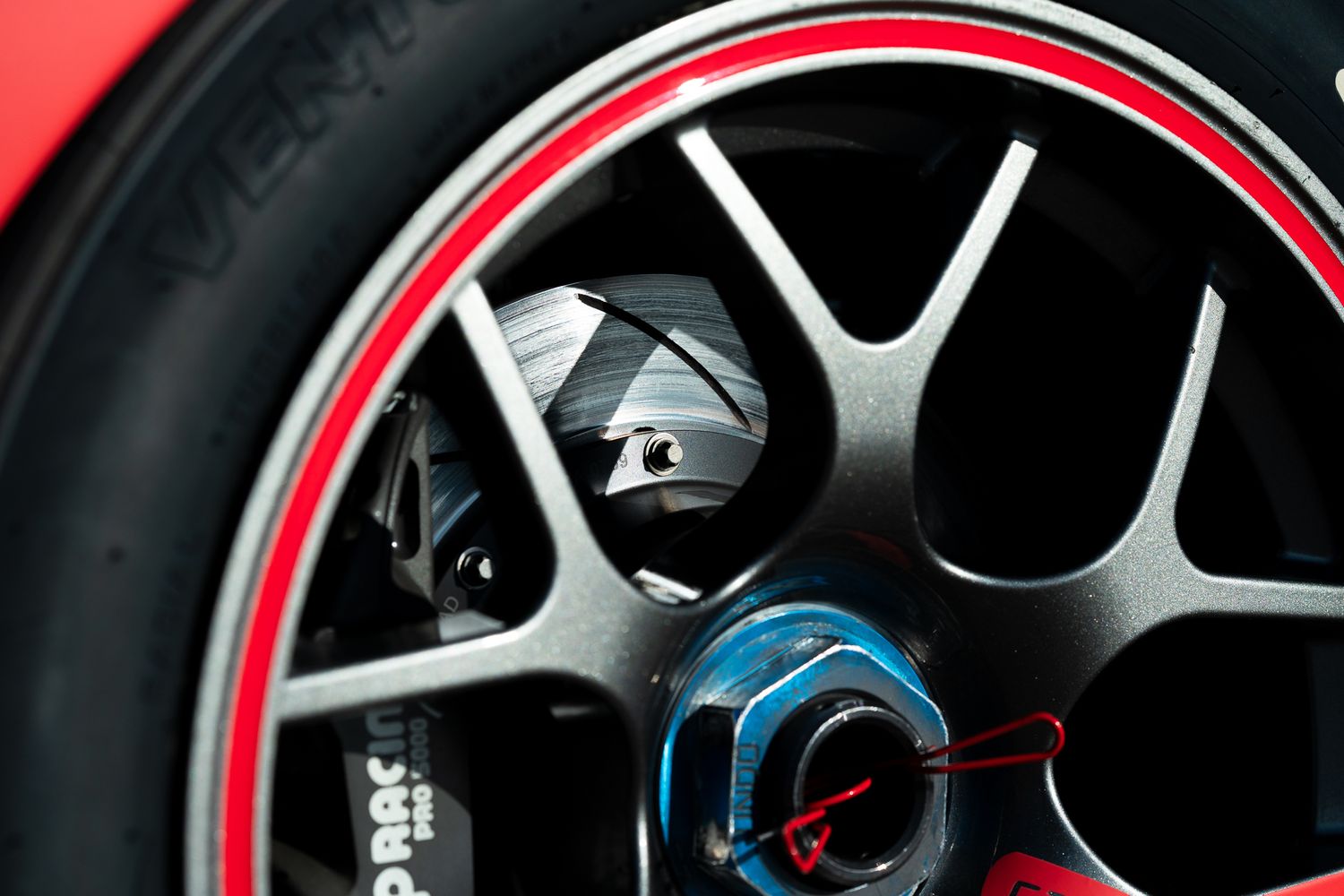 Close-up view of a motorcycle wheel rim with red accent stripe and silver spokes against a dark background.