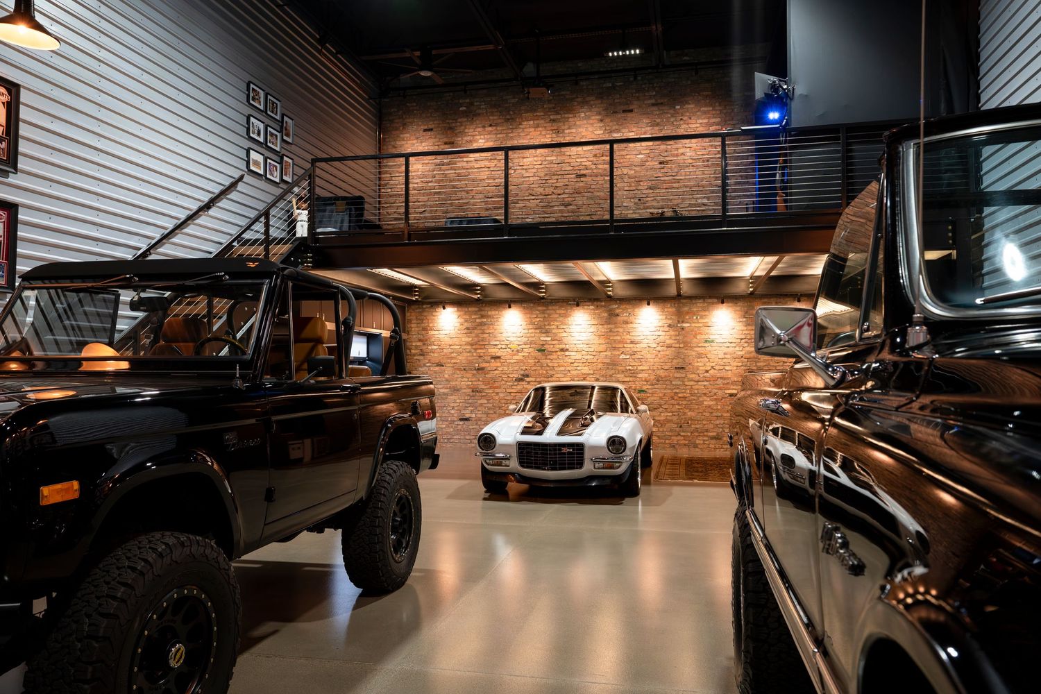 Luxury car collection displayed in modern garage with brick walls and mezzanine level.