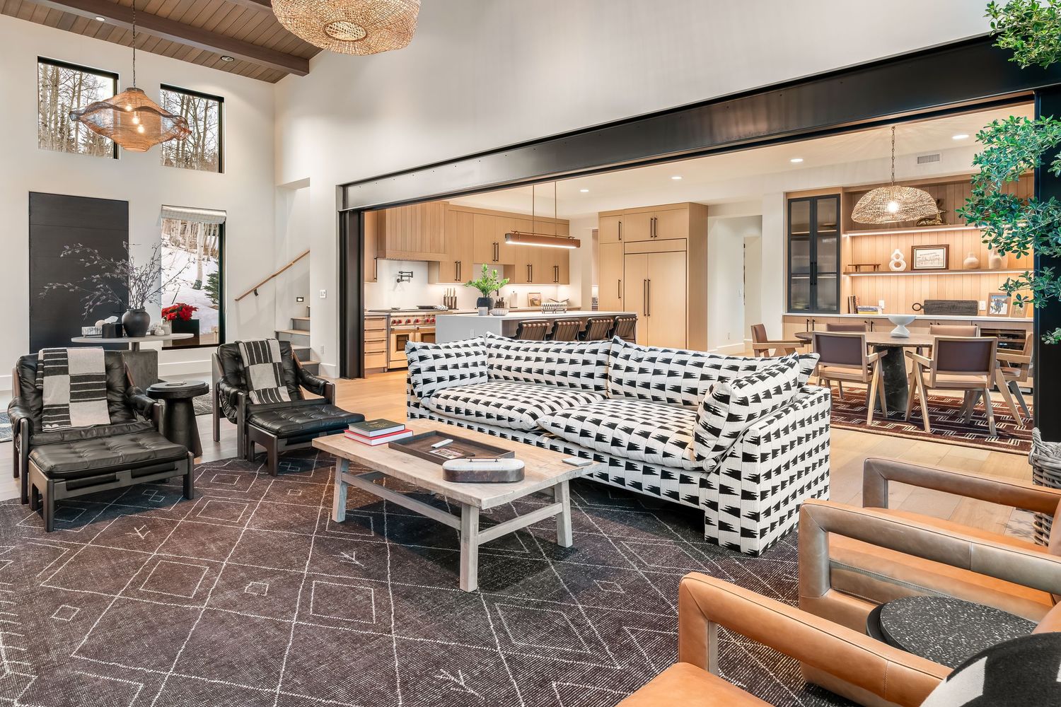 Modern living room with geometric patterned sofa, dark tile flooring, and open concept layout connecting to kitchen area.