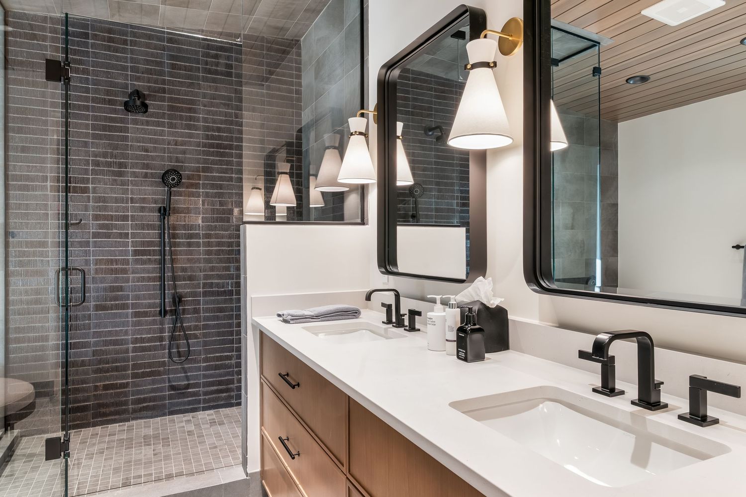 Contemporary bathroom with gray subway tile, black fixtures, and white countertop featuring modern lighting design.