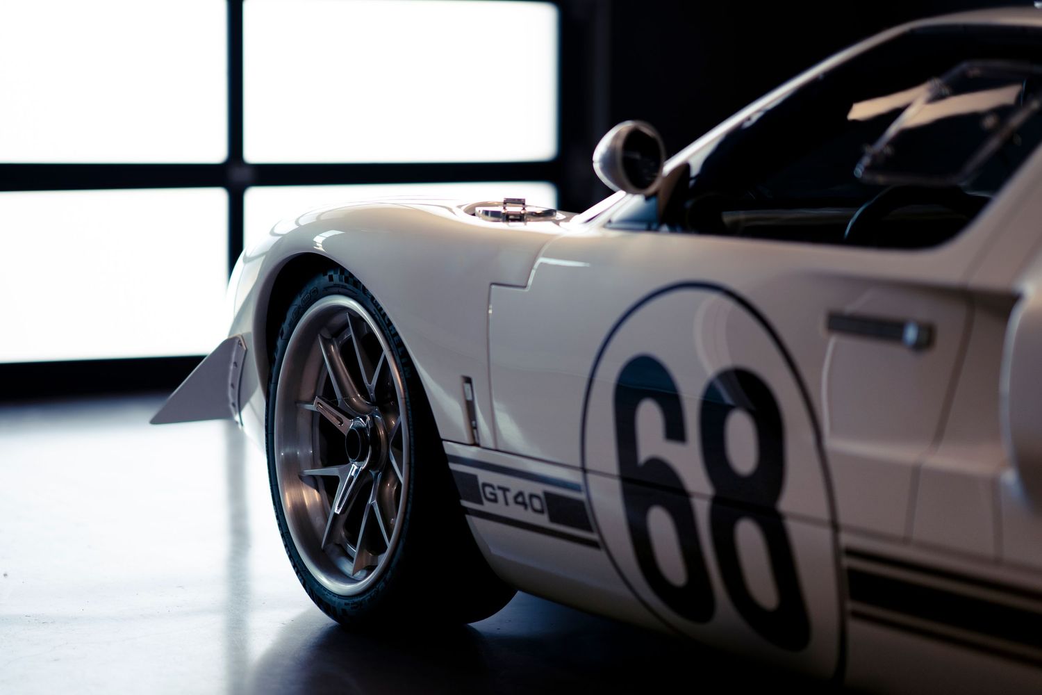 Close-up view of a white racing car with number 68 showing the front wheel and side panel in a showroom setting.