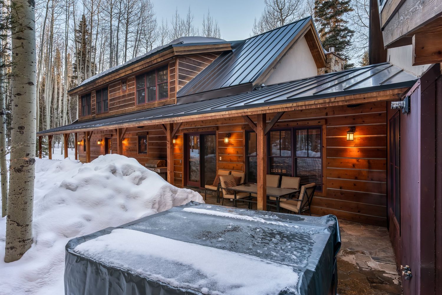 Winter view of a log cabin nestled among snow-covered trees with outdoor lighting and deck features.