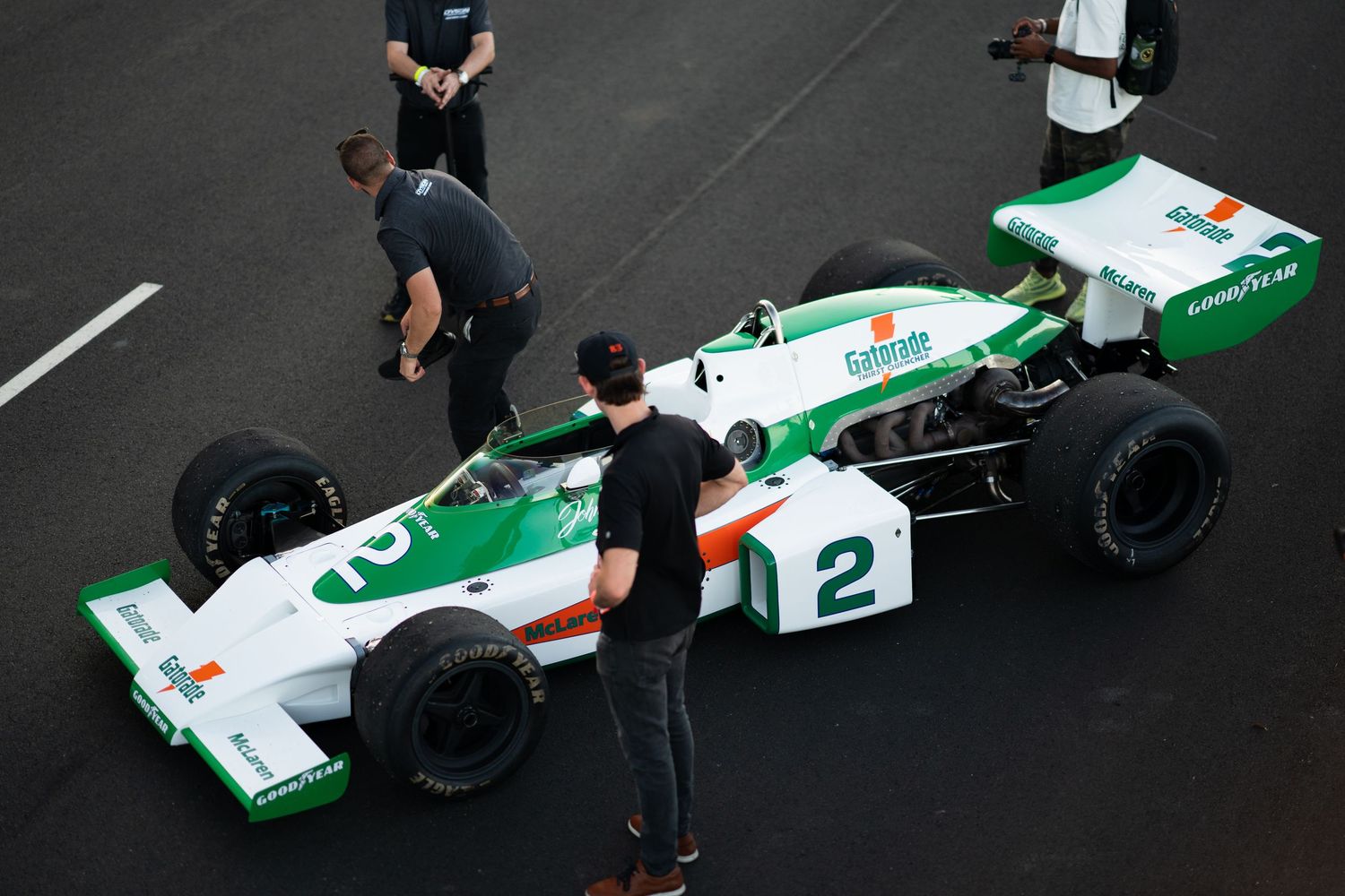 Green and white Formula One race car being worked on by pit crew members in a garage setting.