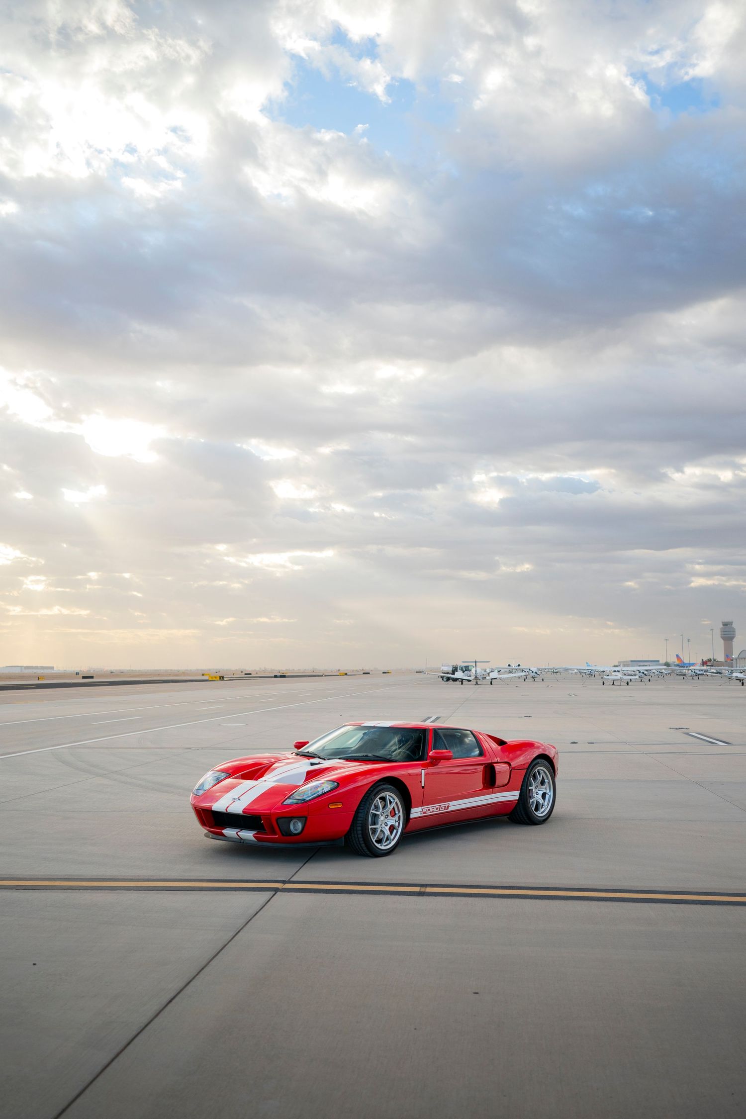 Ford GT sports car on airport tarmac with dramatic cloudy sky above.